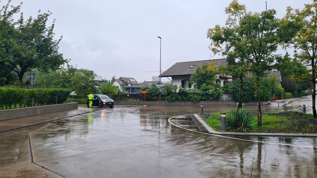 Niederuster ist fast schon gespenstisch leer. Ein Verkehrskadett klärt Unwissende darüber auf, wo sie mit dem Auto hinkommen und wo nicht. Ein Kreisel, im Hintergrund ein Auto und ein Mann in gelben Leuchtkleidern.